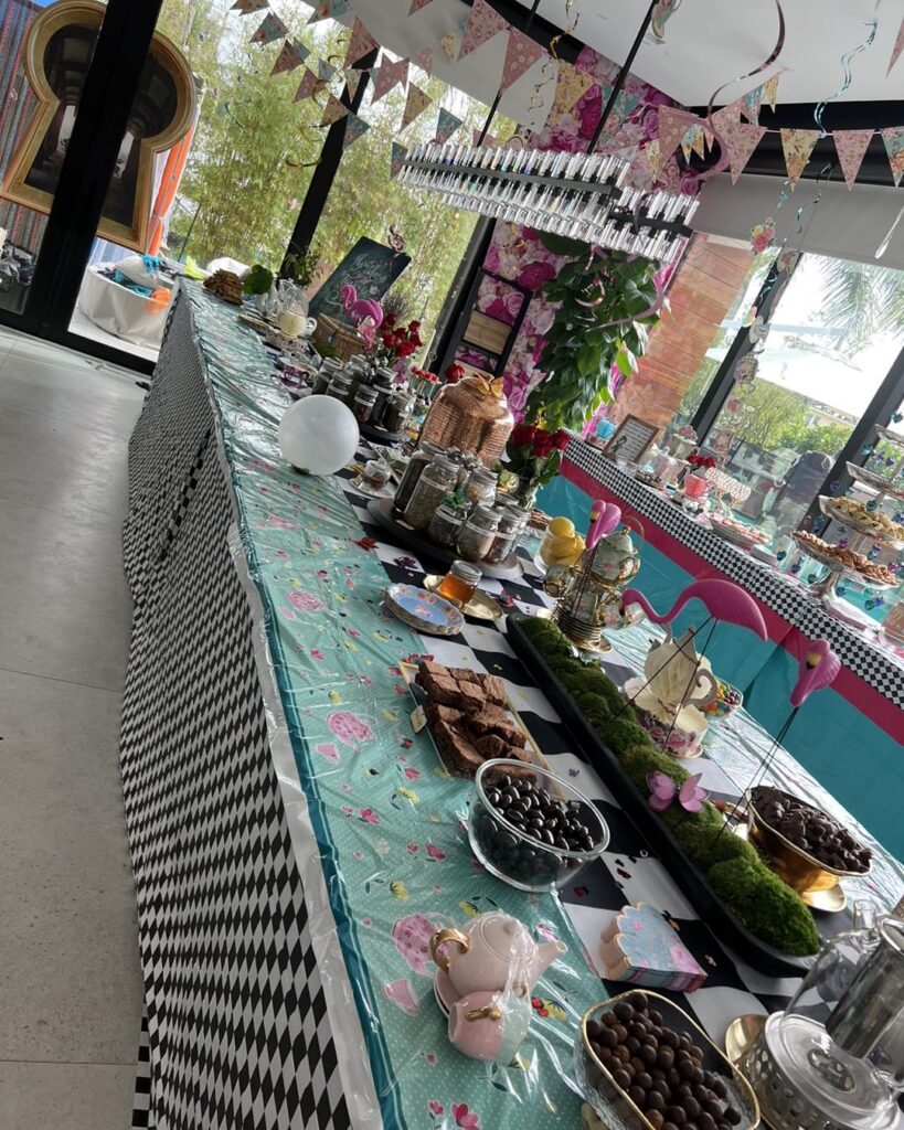 A long table set for an adult party extravaganza, adorned with colorful decorations, assorted foods, and a black and white checkered tablecloth.