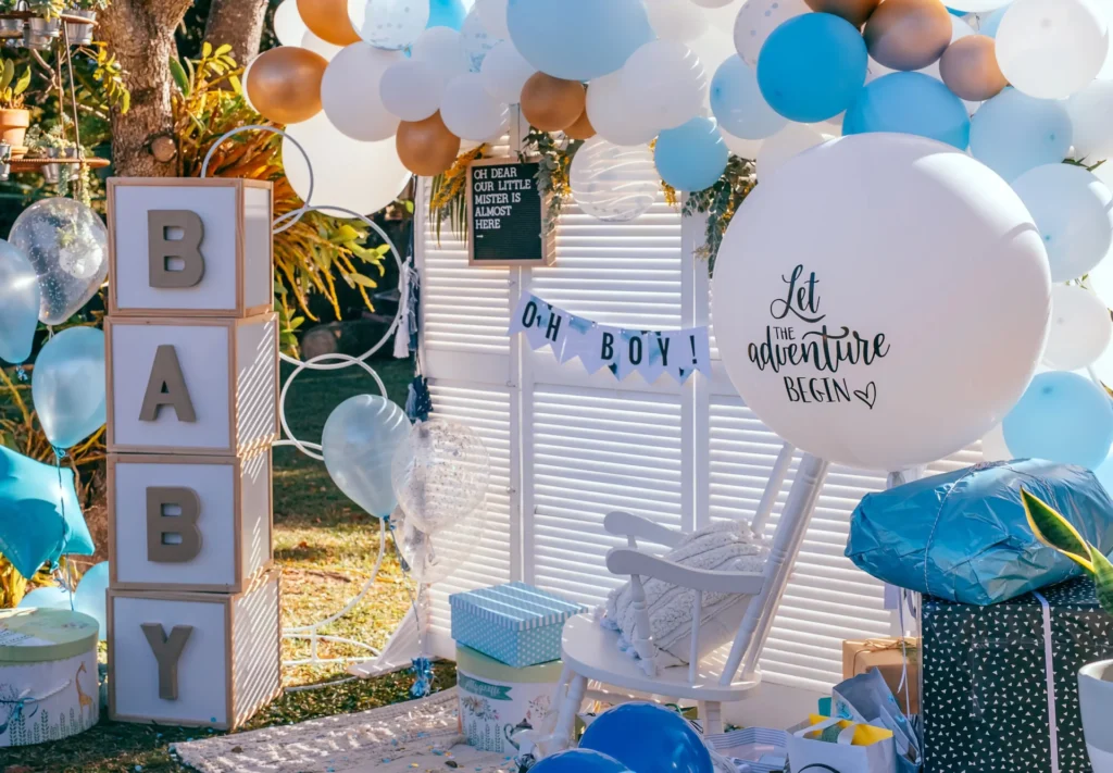 Decorated outdoor baby shower with "baby" block letters, balloons, and gifts in a blue and white color scheme, featuring signs saying "oh boy!" and "let the adventure begin," now with