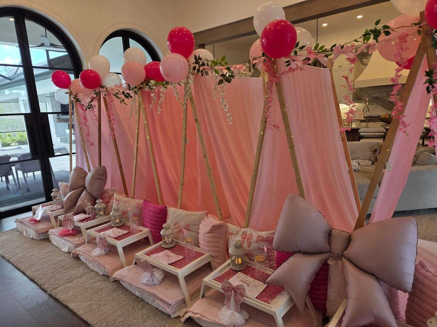 Pink teepee sleepover party setup with balloon garlands and breakfast trays